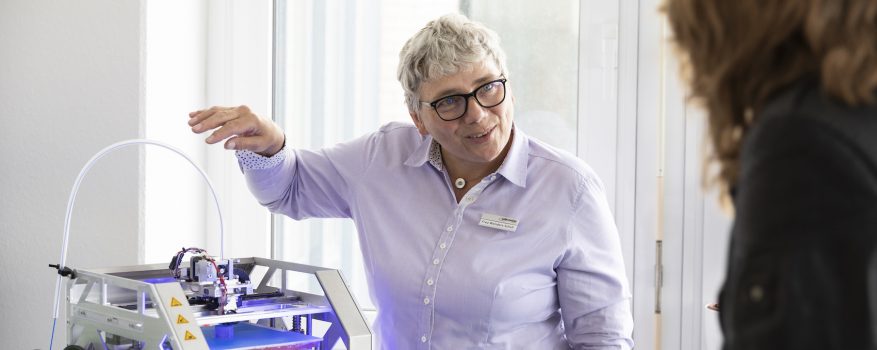 Barbara Wenders-Scholl trägt Brille und kurze graue Haare und steht neben 3D-Drucker.