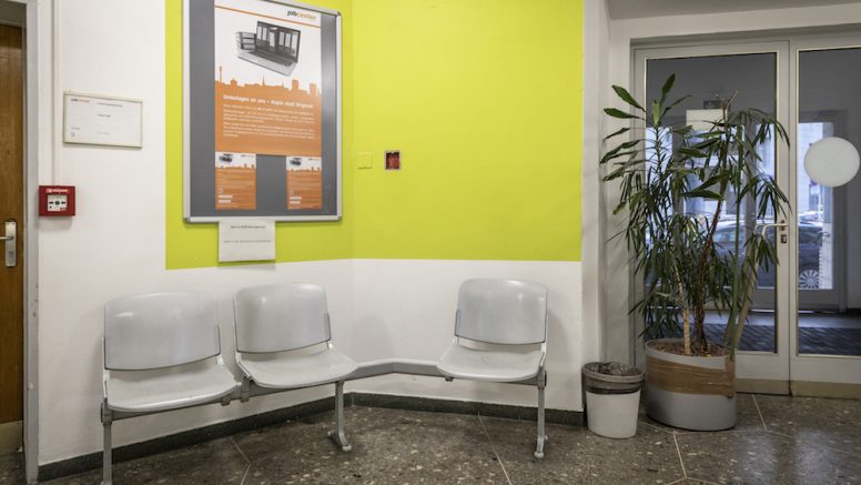 Eingangsbereich des Jobcenters mit drei Stühlen und einer gelben Wand