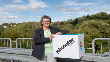 Martina Kober, Geschäftsführerin des Jobcenters Vogtland, hält lächelnd einen großen Würfel mit der Aufschrift Jobcenter Vogtland in der Hand.