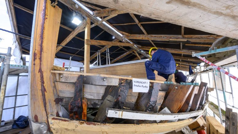 Ein Mann in Blaumann arbeitet am Holzgestell des Schiffes.