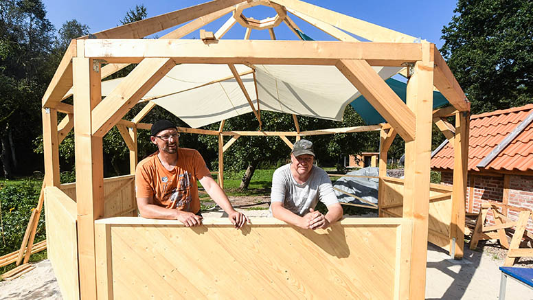 Zwei Männer stehen im Rohbau des Pavillons, der aus einem achteckigen Holzgestell besteht.