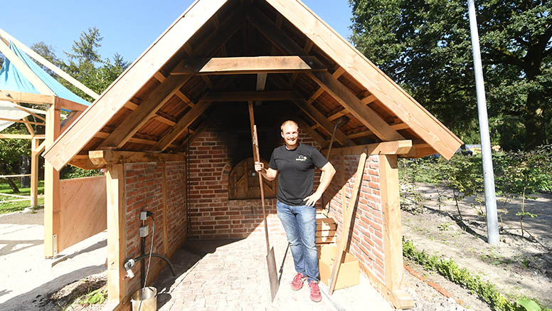 Ein Mann steht unter dem Backhause, das Backsteinwänden und Holzdach hat.