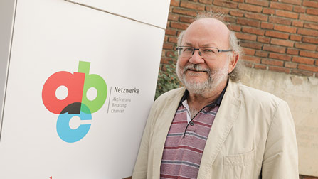 Claus Reis hat graue Haare und steht neben einem Schild mit dem Logo der Netzwerke ABC.OeffnetSeiteIm Gespräch mit Prof. Dr. Claus Reis
