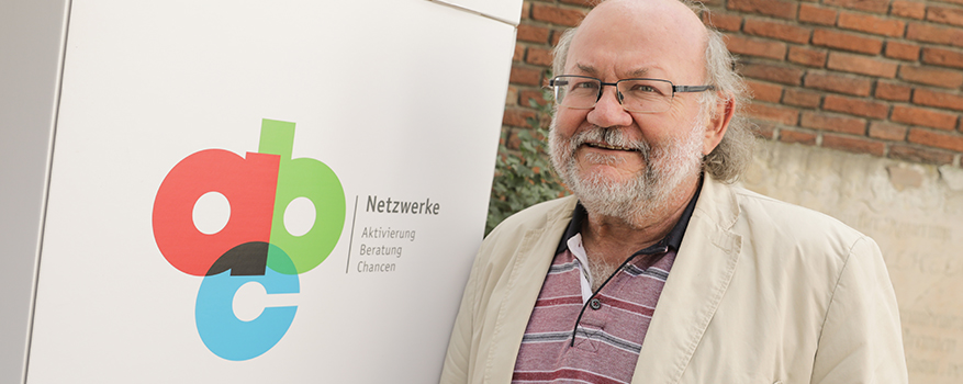Claus Reis hat graue Haare und steht neben einem Schild mit dem Logo der Netzwerke ABC.