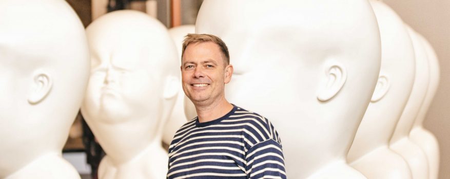 Stefan Stahl steht neben weißen mannshohen Kunststatuen, die an Babys erinnern.
