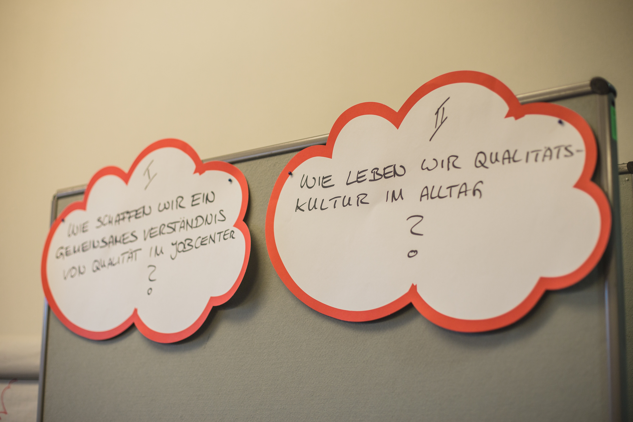 Zwei Moderationskarten in Wolkenform mit Fragen darauf hängen an einer Metaplanwand (ausgwähltes Bild)