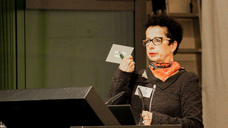 Eine Frau mit Brille steht hinter einem Rednerpult (Bild anzeigen)
