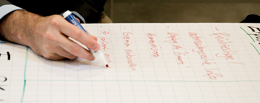 Nahaufnahme einer Hand, die mit rotem Filzstift Stichpunkte auf ein Papier schreibt