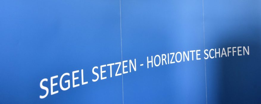 Ein dunkelblaues Wandbild zeigt die Wahrzeichen Kiels. Darunter steht der Satz: Segel setzen – Horizonte schaffen.