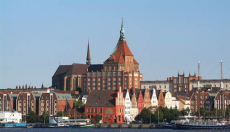 Sicht auf eine emporragende gotische Kirche sowie Häuser in hanseatischer Bauweise am Meer.