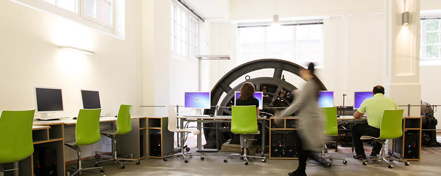 Das Coachingzentrum in einem hellen alten Fabrikraum mit hohen Wänden und grünen Stühlen an PCs 