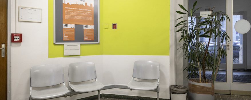 Eingangsbereich des Jobcenters mit drei Stühlen und einer gelben Wand