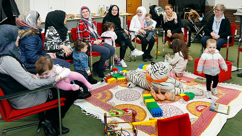 Frauen sitzen im Stuhlkreis. Kinder sitzen auf den Schößen oder spielen in der Mitte auf dem Boden.