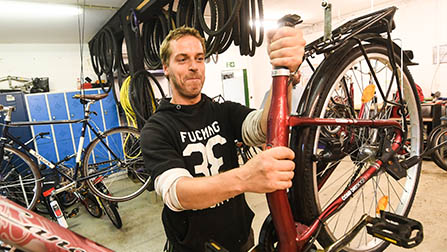Ein Mann in schwarzem Kapuzenpullover hält ein Fahrrad hoch in der Fahrradwerkstatt. (ausgwähltes Bild)