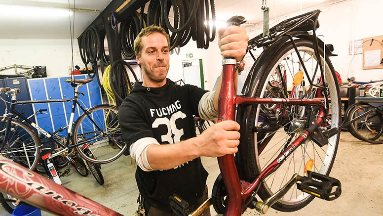 Ein Mann in schwarzem Kapuzenpullover hält ein Fahrrad hoch in der Fahrradwerkstatt.