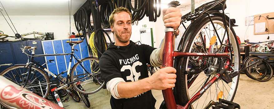Ein Mann in schwarzem Kapuzenpullover hält ein Fahrrad hoch in der Fahrradwerkstatt.
