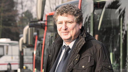 Porträtfoto von Ralf Greulich. Er hat kurze graue Locken und ein rundes Gesicht. Er steht vor geparkten Bussen. (Bild anzeigen)