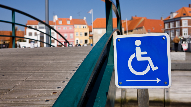 Blaues Straßenverkehrsschild mit Rollstuhlsymbol an einer Brücke.