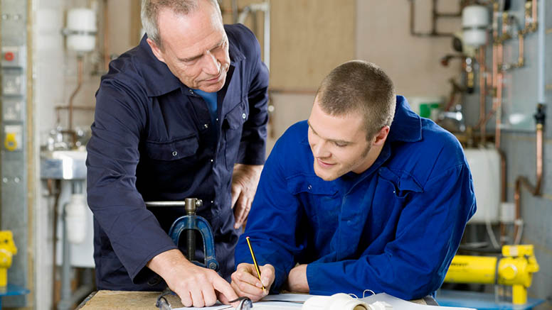 Ein Meister hilft einem jungen Mann in der Werkstatt beim Zeichnen.