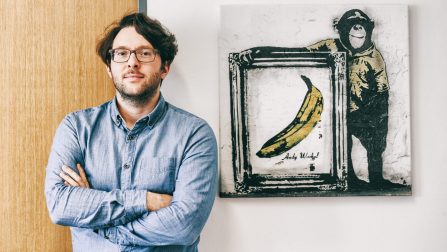 Alexander Scheungrab steht neben einem Bild in Graffiti-Style, das einen Affen und die Warhol-Banane zeigt.Öffnet Seite: Maximale Transparenz