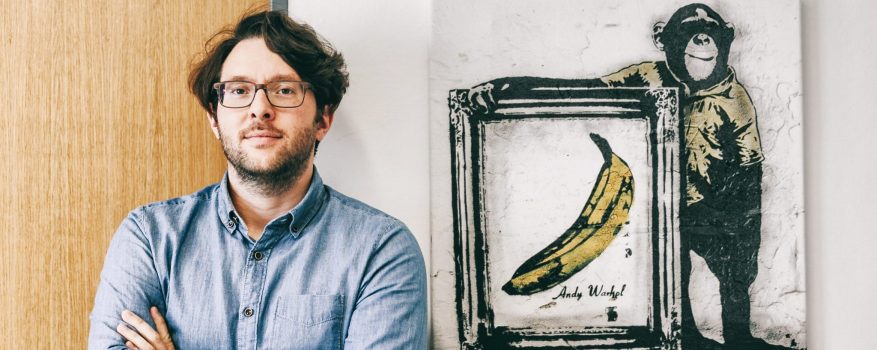 Alexander Scheungrab steht neben einem Bild in Graffiti-Style, das einen Affen und die Warhol-Banane zeigt.