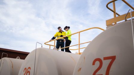 Eine Frau und ein Mann in gelben Warnwesten stehen auf einem Tank mit gelbem Geländer.Öffnet Seite: Sozialer Arbeitsmarkt